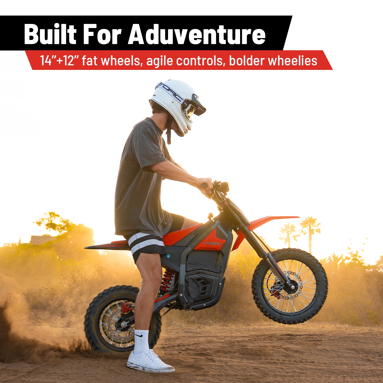 A dynamic image featuring the Yozma IN 10 Electric Mini Dirt Bike in action, with a rider performing a wheelie on a dirt track, kicking up dust at sunset. Prominent text declares "Built For Adventure" and highlights key features: "14"+12" fat wheels, agile controls, bolder wheelies."